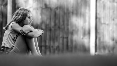 Side view of thoughtful girl hugging knees while sitting against wall