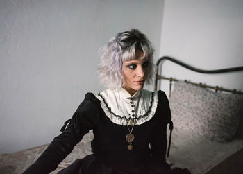 Thoughtful woman wearing costume while sitting on bed wall at home