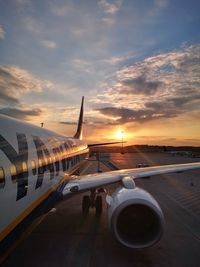 Airplane on airport runway against sky during sunset