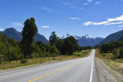 Empty road along trees and mountains against sky