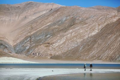 People standing on beach against mountains