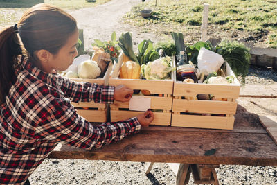 Mature female farmer sticking label on crate full of vegetables at market