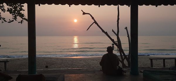 Rear view of silhouette man on beach against sky during sunset