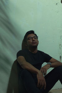 Young man looking away while sitting on wall