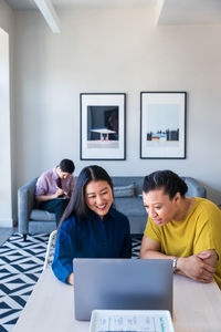 Smiling female entrepreneurs planning strategy over laptop while male colleague sitting on sofa at office