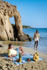 Friends on rock at beach against clear sky