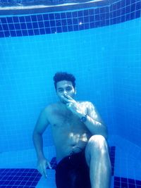 Portrait of shirtless young man sitting in swimming pool