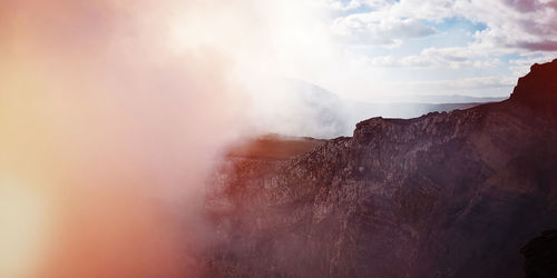 Smoke emitting from mountain against sky