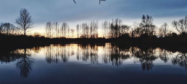 Reflection of silhouette trees in lake against sky during sunset