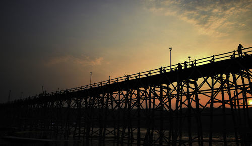 Silhouette bridge over river against sky during sunset