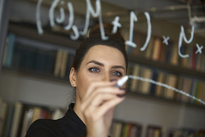 Businesswoman writing formula on glass wall at office