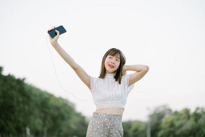 Young woman holding smart phone and looking away while standing on land