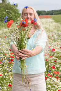 Beautiful middle-aged blonde woman stands among a flowering field of poppies