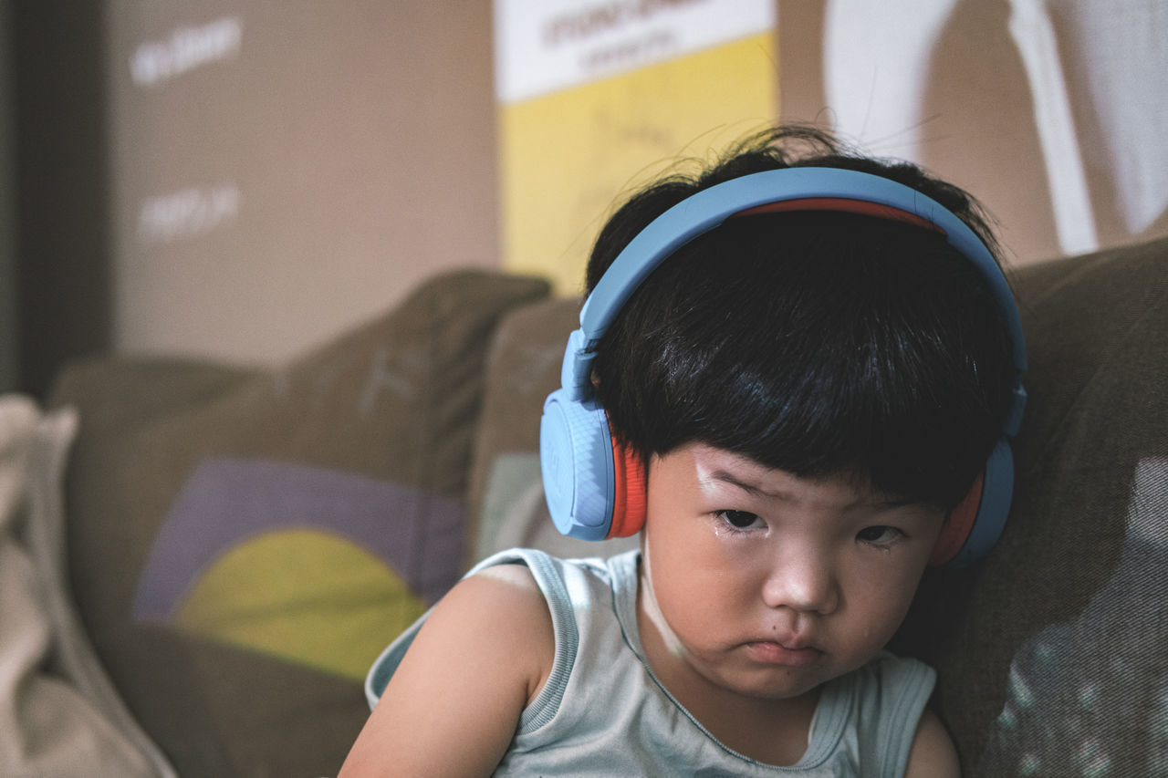 child, childhood, headphones, one person, portrait, indoors, men, listening, domestic room, lifestyles, innocence, furniture, music, person, front view, relaxation, sitting, domestic life, casual clothing, skin, leisure activity, looking, toddler, sofa, home interior, living room, serious, baby, blue, headshot, bed, emotion, focus on foreground, cute, day, bedroom, human face