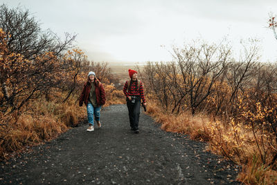 Young happy tourists in winter wear going on forest road and cloudy sky