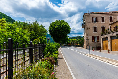 Road by trees against sky in city