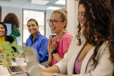 Happy mature female entrepreneur sitting with colleagues during meeting at office