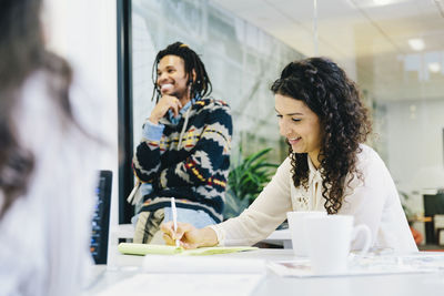 Businesswoman writing on note pad while working with colleagues in conference room