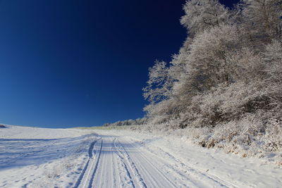 Snow covered landscape against clear blue sky