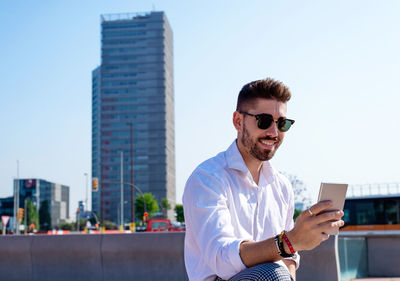 Young bearded man sits on bench outdoor against modern glass building