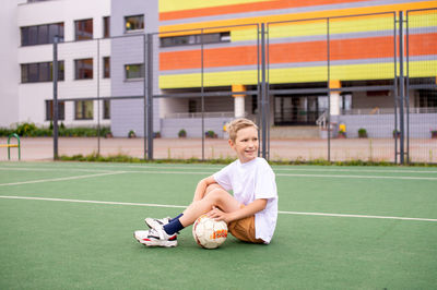 A boy holds a soccer ball while sitting on a soccer field