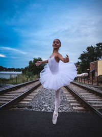 Ballet dancing by railroad tracks against sky