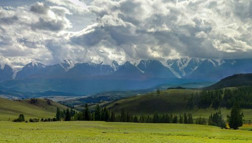 Scenic view of grassy field and mountains against cloudy sky