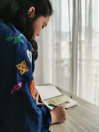 Side view of young woman reading book while sitting on table