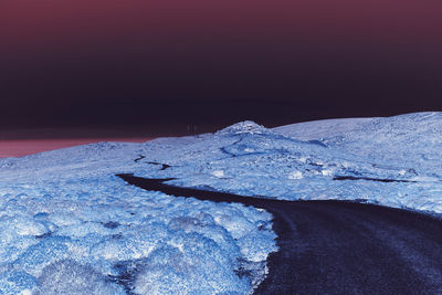 Snow on sea shore against sky during sunset