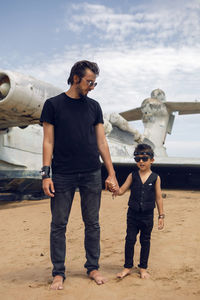 Family boy and his father in rocker clothes stand an abandoned ekranoplan plane by sea in dagestan