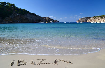 Ibiza text on wet shore against clear blue sky