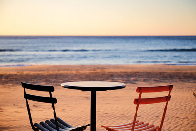 Empty chairs on beach against sky during sunset