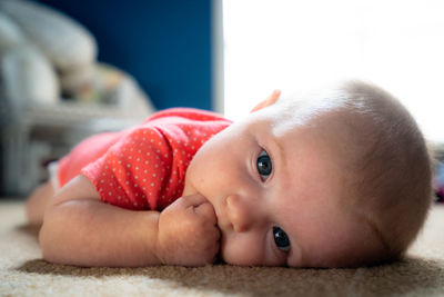 Portrait of cute baby girl hand covering mouth while lying on carpet
