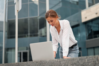 Close-up of smiling businesswoman using laptop standing outdoors