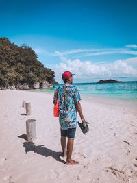 Rear view of man walking at beach against sky