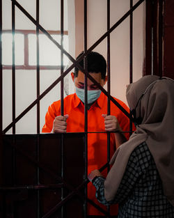 Rear view of man standing by railing, love separated by cage