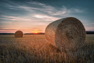 Hay bales on field against sky during sunset