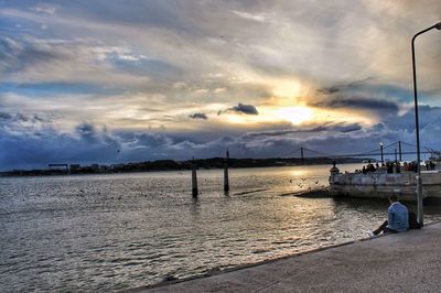 Rear view of man sitting on harbor against sky during sunset