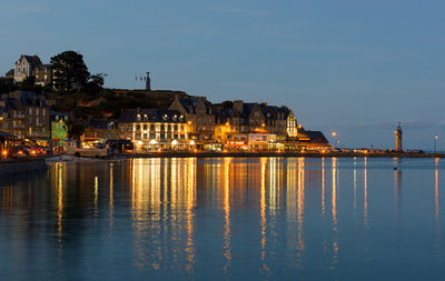 Illuminated buildings by sea against sky at dusk