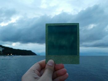 Cropped hand holding photograph in front of sea