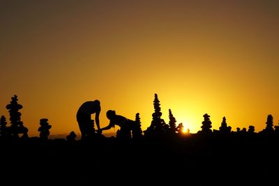 Silhouette people by stones against orange sky during sunset