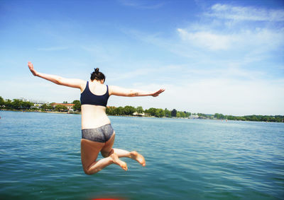 Young woman jumping in sea against blue sky