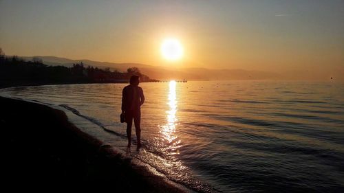 Silhouette woman standing on beach against sky during sunset