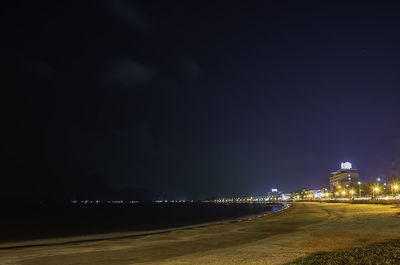 Illuminated buildings by sea against sky at night