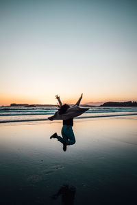 Woman jumping at beach against sky during sunset