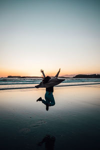 Rear view of man on beach against sky during sunset