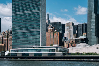 Modern buildings by river against sky in city