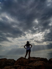 Rear view of woman standing on rock at sea against sky