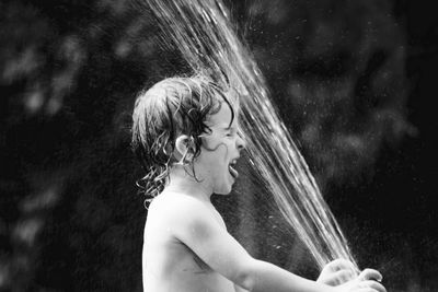 Side view of shirtless boy playing with fountain water
