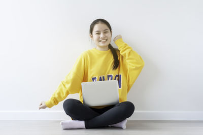 Young woman using phone while sitting on white background